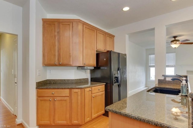 kitchen with sink, light hardwood / wood-style flooring, ceiling fan, black fridge with ice dispenser, and dark stone counters