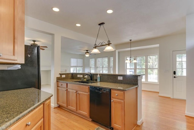 kitchen featuring sink, light wood-type flooring, pendant lighting, dark stone counters, and black appliances