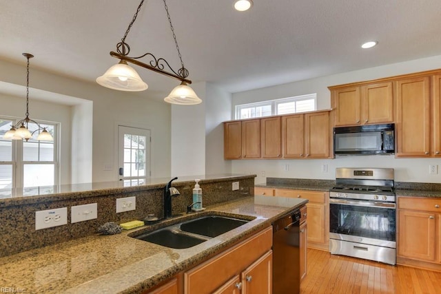 kitchen featuring decorative light fixtures, sink, dark stone counters, black appliances, and light hardwood / wood-style flooring