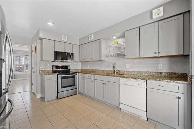 kitchen featuring appliances with stainless steel finishes, stone countertops, tasteful backsplash, sink, and gray cabinetry