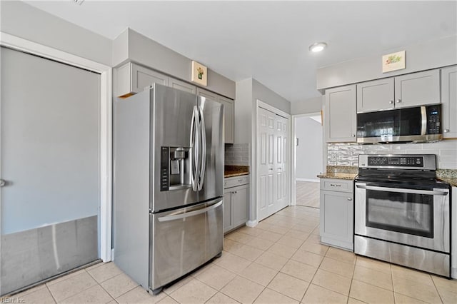 kitchen with light tile patterned floors, gray cabinets, appliances with stainless steel finishes, dark stone countertops, and tasteful backsplash