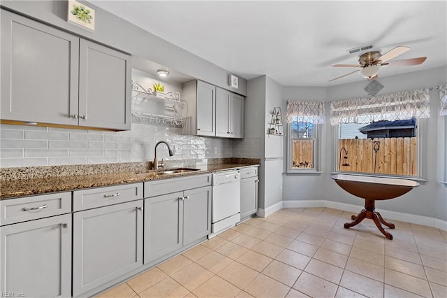 kitchen featuring sink, dark stone countertops, decorative backsplash, light tile patterned floors, and white dishwasher