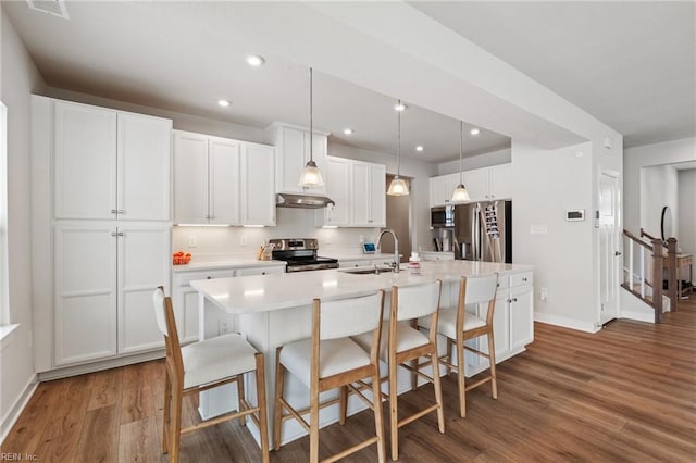 kitchen with sink, dark wood-type flooring, appliances with stainless steel finishes, white cabinetry, and a kitchen island with sink