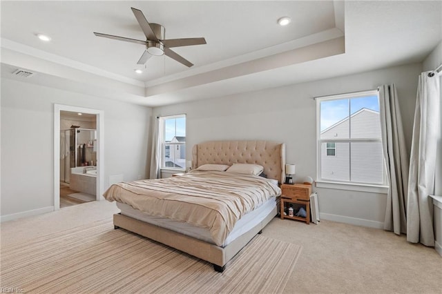 bedroom featuring a raised ceiling, connected bathroom, light colored carpet, and ceiling fan