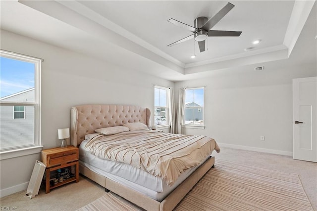 bedroom with ceiling fan, light colored carpet, and a tray ceiling