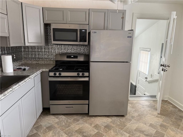 kitchen with tasteful backsplash, stainless steel appliances, sink, and gray cabinetry