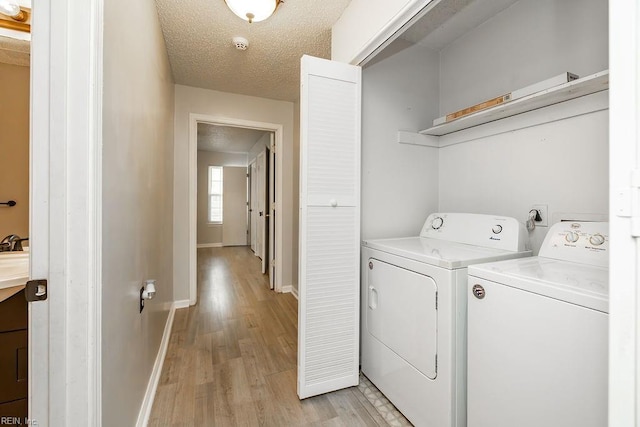 clothes washing area featuring light wood-type flooring, washing machine and clothes dryer, and a textured ceiling