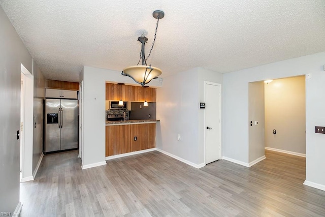 kitchen featuring appliances with stainless steel finishes, decorative light fixtures, decorative backsplash, kitchen peninsula, and light wood-type flooring