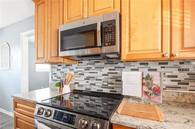 kitchen with tasteful backsplash, light stone counters, and appliances with stainless steel finishes