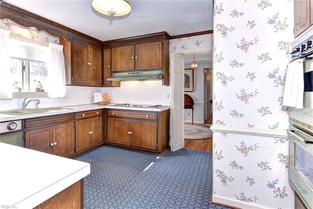 kitchen with wallpapered walls, white stovetop, light countertops, under cabinet range hood, and a sink