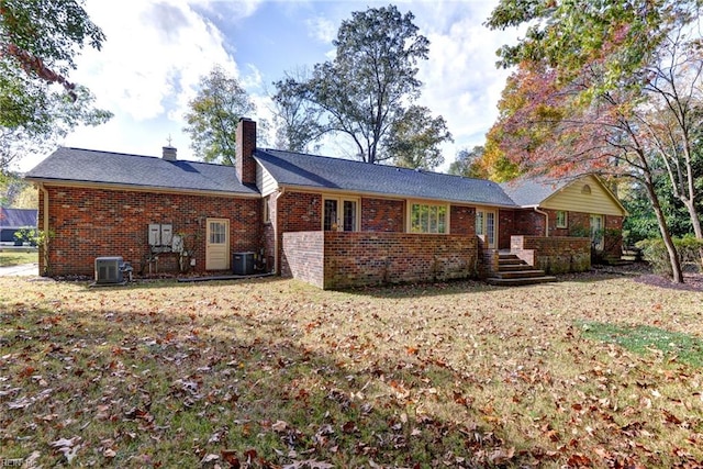 back of house featuring central AC, brick siding, a lawn, and a chimney