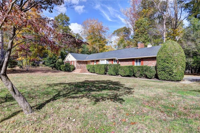 ranch-style home featuring brick siding, a chimney, and a front yard