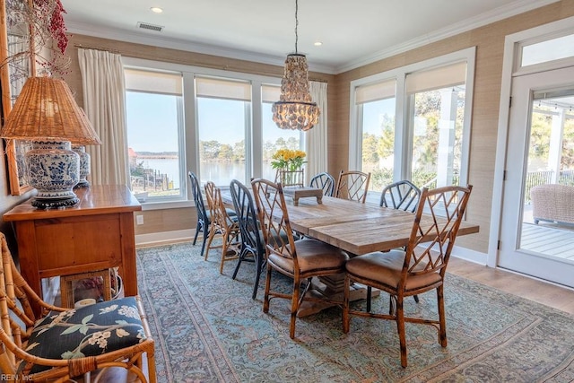 dining area featuring a water view, ornamental molding, a chandelier, and light hardwood / wood-style floors