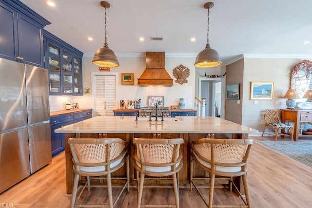 kitchen with blue cabinetry, custom range hood, stainless steel refrigerator, and light wood-type flooring