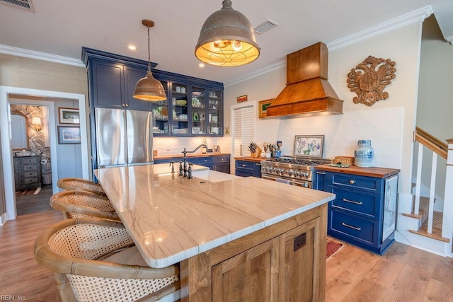 kitchen with blue cabinets, sink, light hardwood / wood-style flooring, appliances with stainless steel finishes, and custom range hood