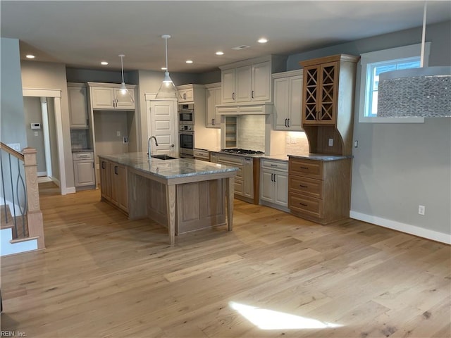 kitchen with a kitchen island with sink, sink, decorative backsplash, and light stone countertops