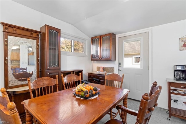 carpeted dining area with vaulted ceiling