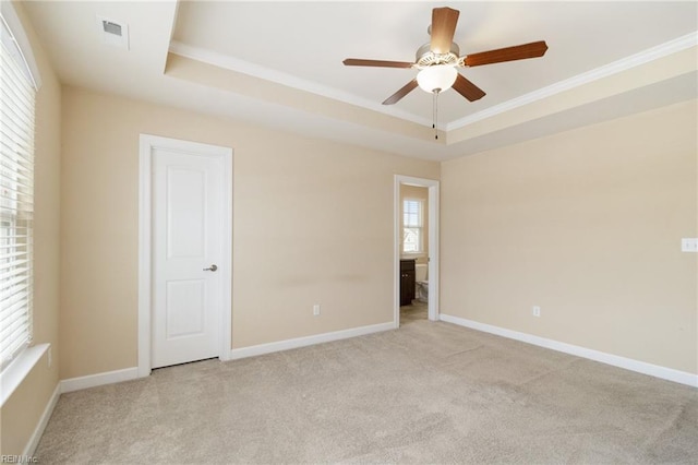 spare room featuring a raised ceiling, ornamental molding, light colored carpet, and ceiling fan