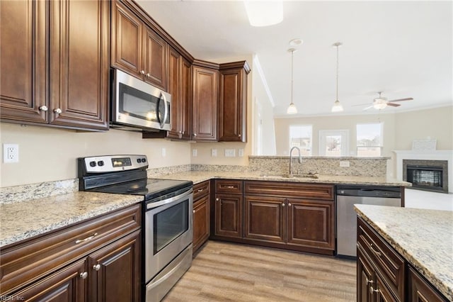 kitchen with decorative light fixtures, sink, ornamental molding, stainless steel appliances, and light wood-type flooring