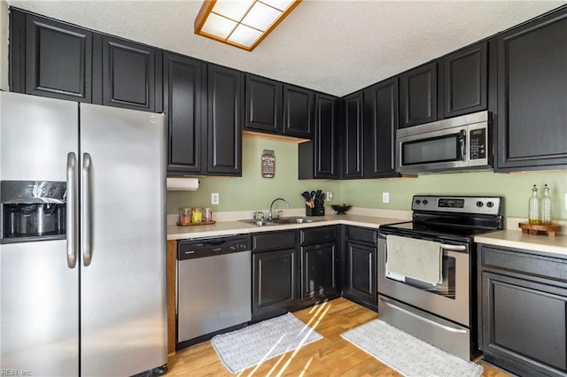 kitchen with stainless steel appliances, sink, a textured ceiling, and light hardwood / wood-style floors