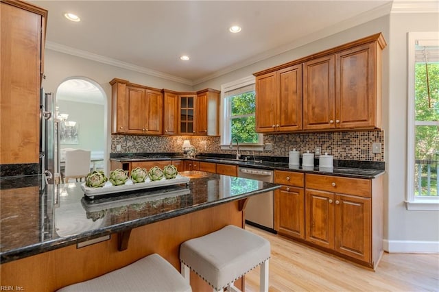 kitchen with a breakfast bar area, light wood-type flooring, dark stone countertops, stainless steel dishwasher, and plenty of natural light