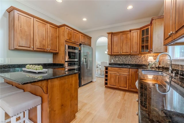 kitchen featuring sink, ornamental molding, appliances with stainless steel finishes, dark stone counters, and light hardwood / wood-style floors