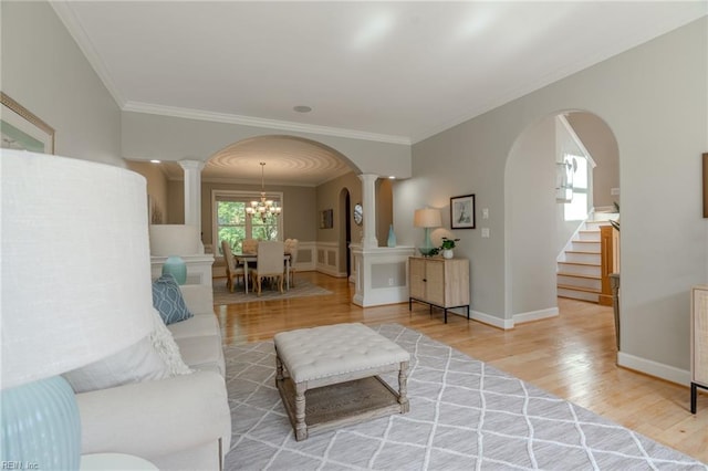 living room featuring hardwood / wood-style floors, a notable chandelier, ornamental molding, and ornate columns