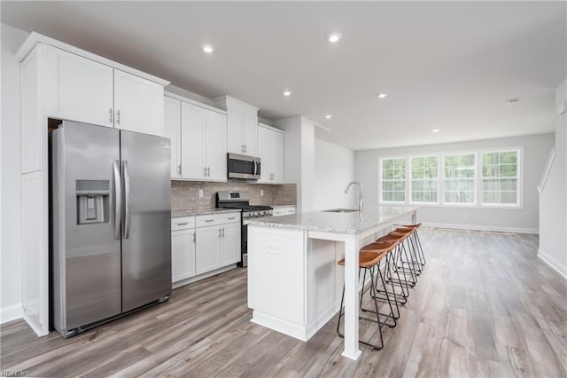 kitchen featuring stainless steel appliances, white cabinetry, light stone countertops, and a center island with sink