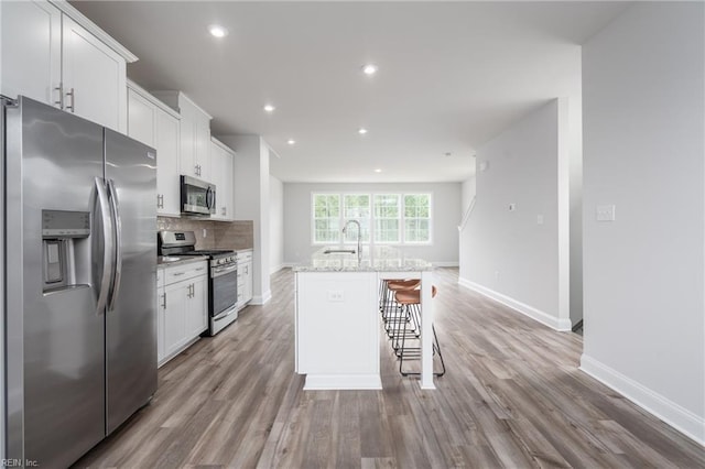 kitchen with an island with sink, white cabinetry, sink, backsplash, and stainless steel appliances