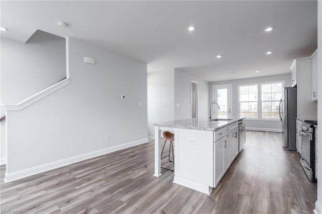 kitchen with white cabinetry, stainless steel appliances, light stone countertops, and a kitchen island with sink