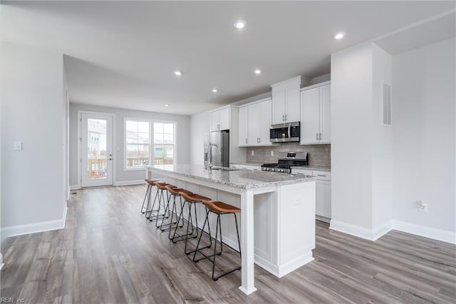 kitchen with a kitchen bar, appliances with stainless steel finishes, an island with sink, light hardwood / wood-style floors, and white cabinets