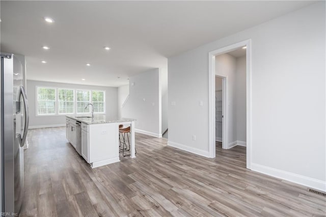 kitchen featuring a breakfast bar area, white cabinetry, stainless steel appliances, light stone countertops, and a center island with sink