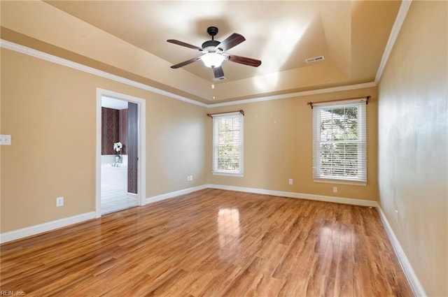 empty room featuring a tray ceiling, ornamental molding, ceiling fan, and light wood-type flooring