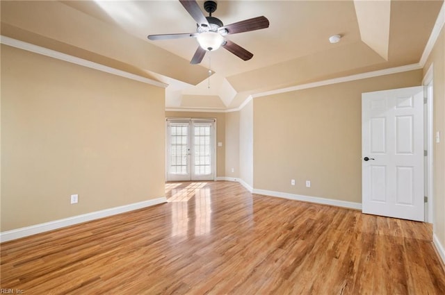 empty room with light hardwood / wood-style floors, ornamental molding, a raised ceiling, and french doors