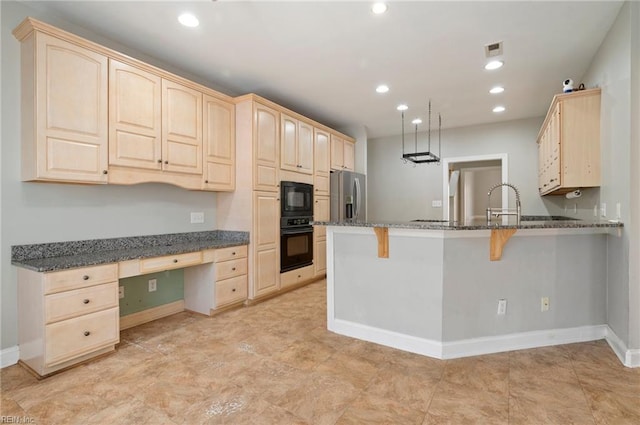 kitchen with built in desk, black appliances, dark stone countertops, a breakfast bar area, and kitchen peninsula