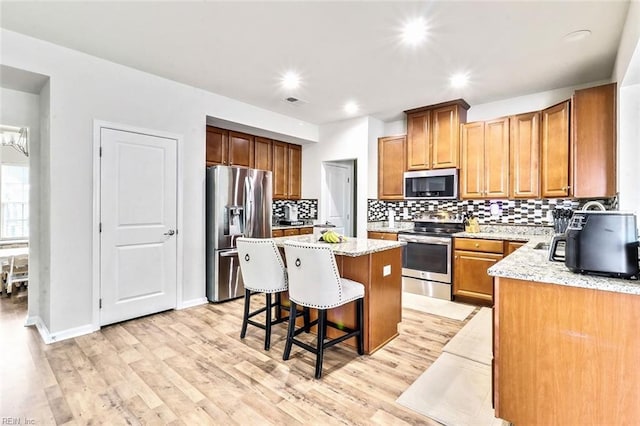 kitchen with a kitchen island, a kitchen bar, light stone counters, stainless steel appliances, and light wood-type flooring