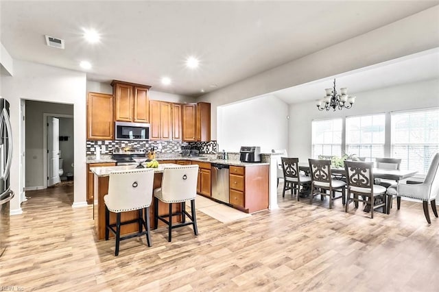 kitchen with a kitchen island, appliances with stainless steel finishes, a chandelier, light stone countertops, and light wood-type flooring