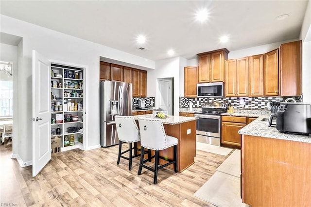 kitchen with light stone countertops, appliances with stainless steel finishes, a center island, and light wood-type flooring