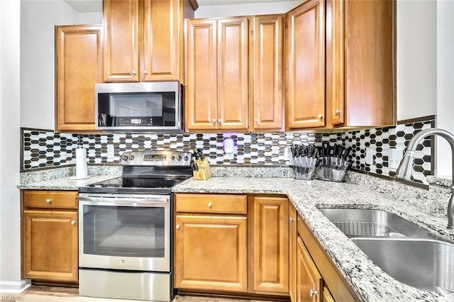 kitchen with stainless steel appliances, light stone countertops, sink, and decorative backsplash