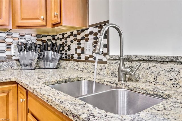 room details featuring tasteful backsplash, sink, and light stone counters