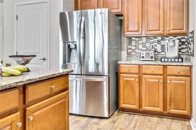 kitchen featuring tasteful backsplash, stainless steel fridge, light stone countertops, and light hardwood / wood-style flooring