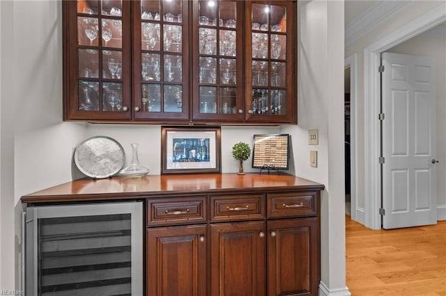 bar with ornamental molding, beverage cooler, and light hardwood / wood-style flooring