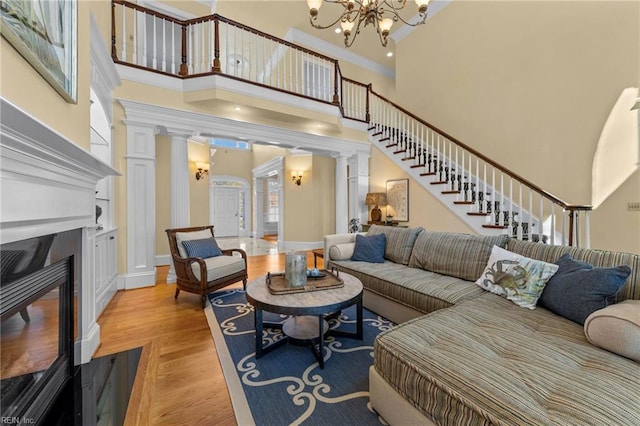 living room with crown molding, light hardwood / wood-style flooring, a towering ceiling, decorative columns, and a chandelier