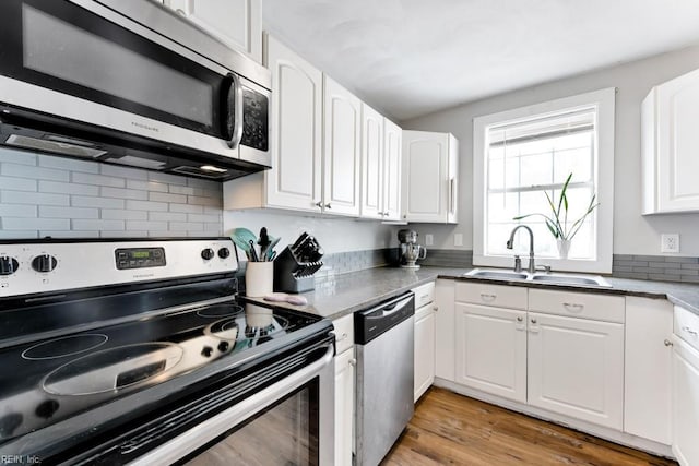 kitchen with appliances with stainless steel finishes, white cabinetry, sink, backsplash, and dark hardwood / wood-style flooring