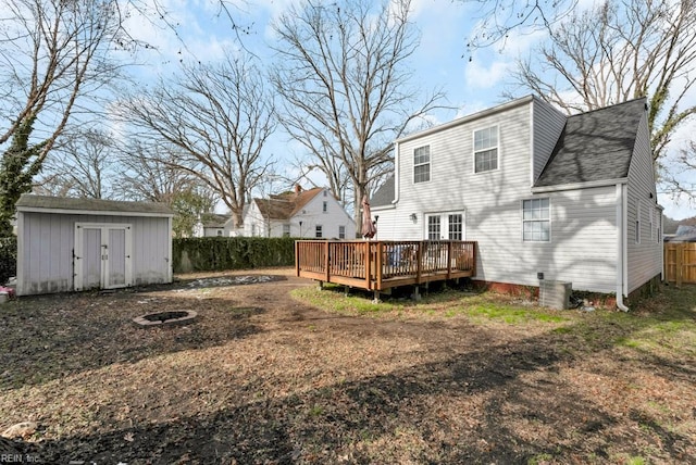 back of property with a wooden deck, an outdoor fire pit, and a shed