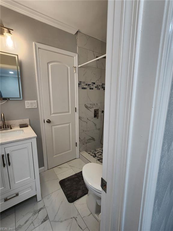 bathroom with vanity, tiled shower, ornamental molding, and toilet