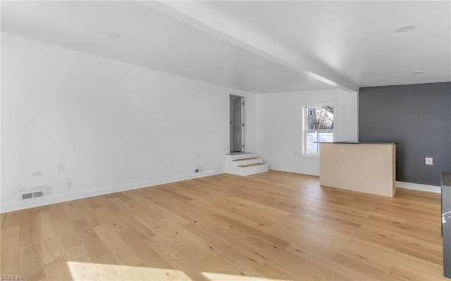 unfurnished living room featuring beamed ceiling and light wood-type flooring