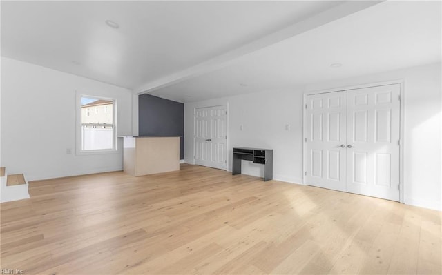 unfurnished living room featuring beamed ceiling and light hardwood / wood-style flooring