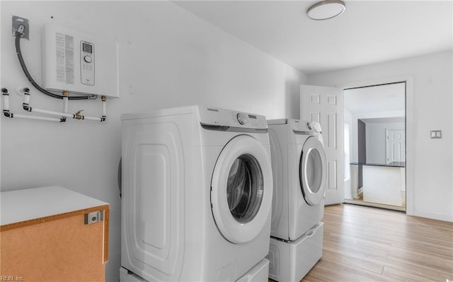 laundry area with water heater, washer and dryer, and light wood-type flooring