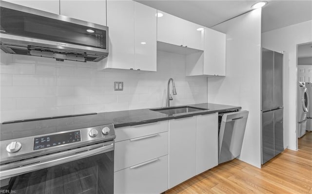 kitchen with sink, light hardwood / wood-style flooring, appliances with stainless steel finishes, dark stone counters, and white cabinets